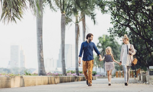 family walking waterfront palm trees holding hands city