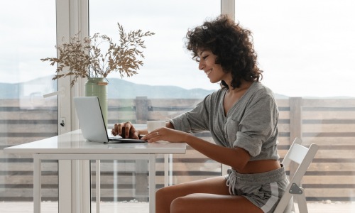 woman sitting table laptop smiling large windows view