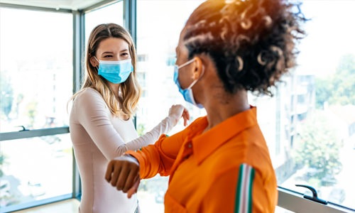 In-Person Tours Two women wearing masks, smiling, and meeting for an in-person tour.